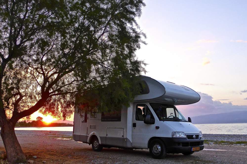 A motorhome parked by a tree with beautiful sunset in the distance